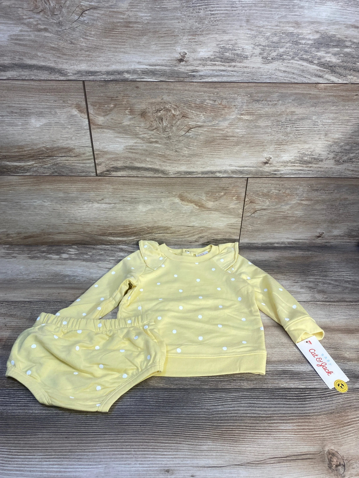 Yellow baby outfit set with white polka dots, long sleeve top and bloomers, on wood background