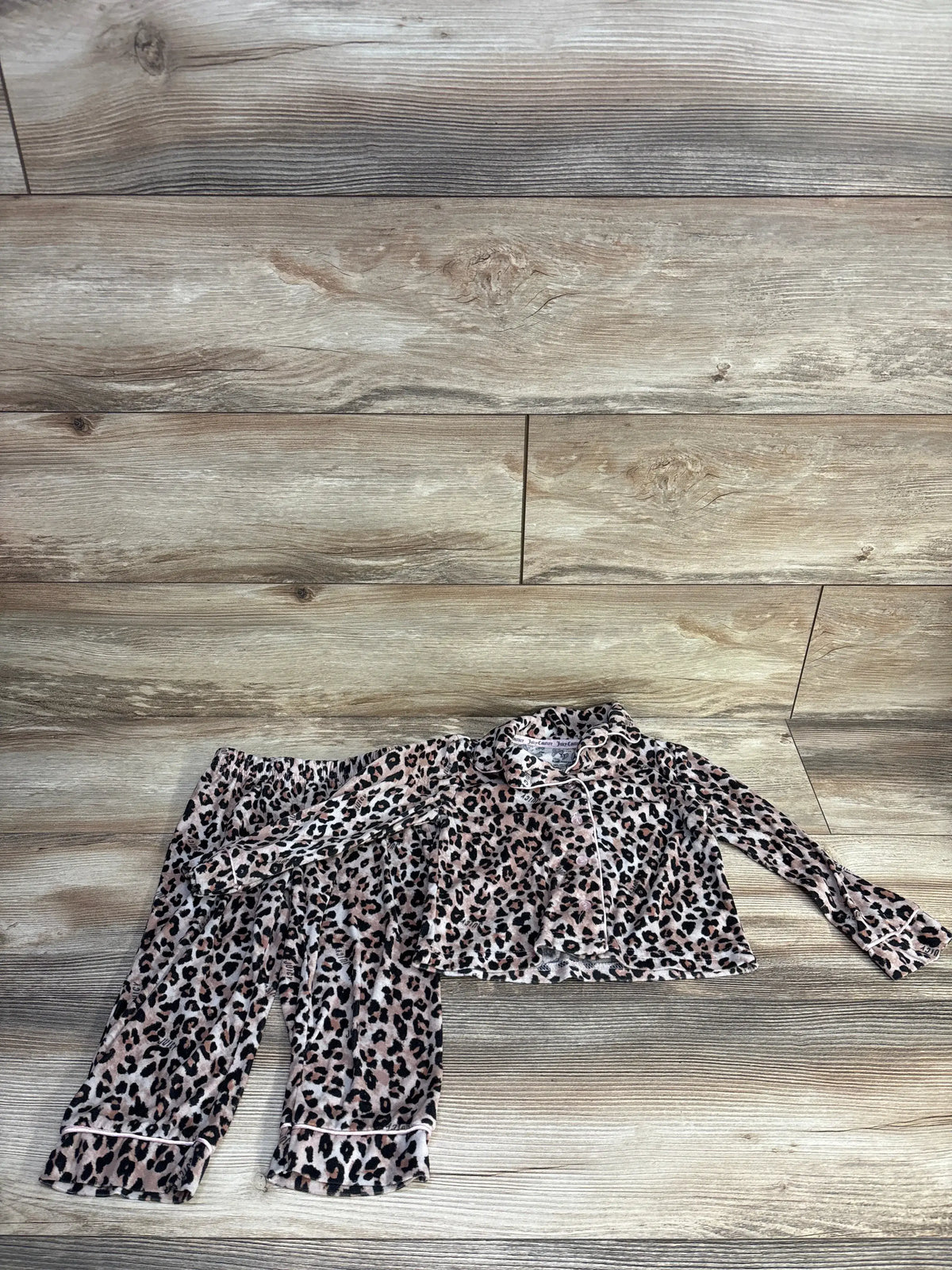 Flat lay of Juicy Couture 2pc leopard coat style pajama set showcasing matching pants and beige leopard print on wood floor