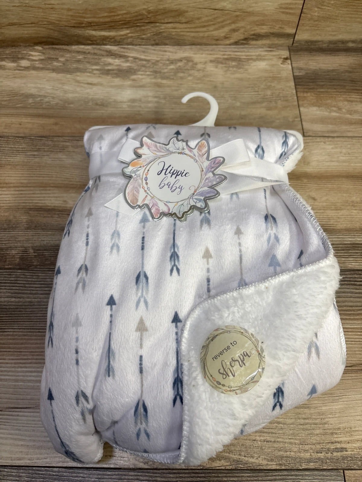 Top view of Hippie Baby reversible blanket in Quinn Arrow Blue showcasing arrow print and fluffy white reverse on wood floor
