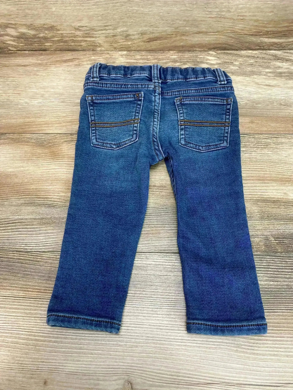 Back view of Carter’s toddler skinny jeans showing elastic waistband and back pockets, blue, size 18M on wood floor