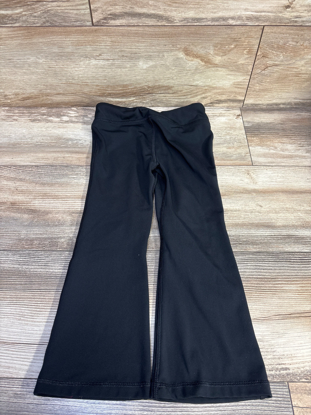 Top-down flat lay of Under Armour flared leggings showcasing flared legs and elastic waistband with light wood floor background
