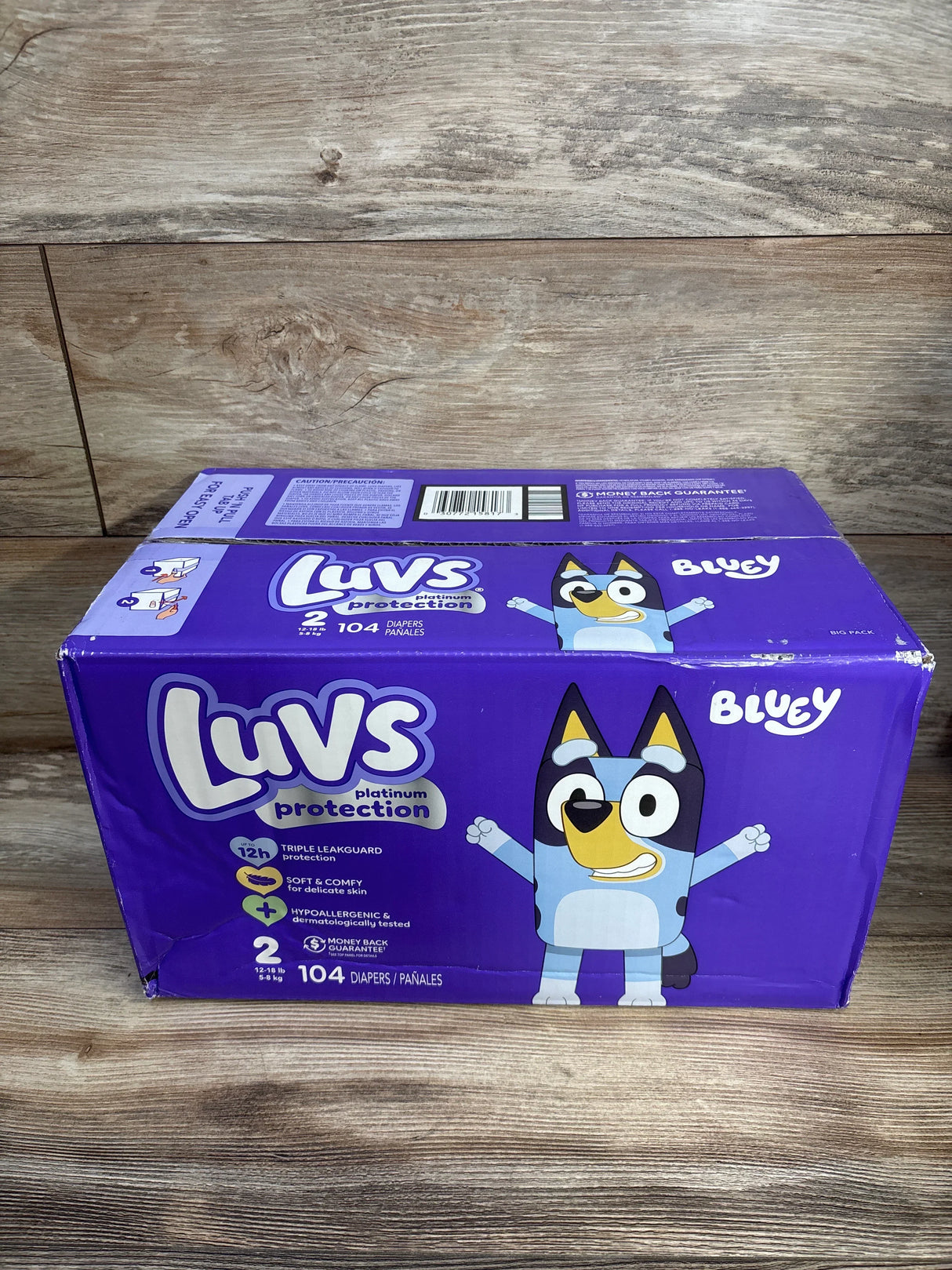 Front view of Luvs Platinum Protection Size 2 diaper box (104 count) showing Bluey character and branding on wooden tabletop