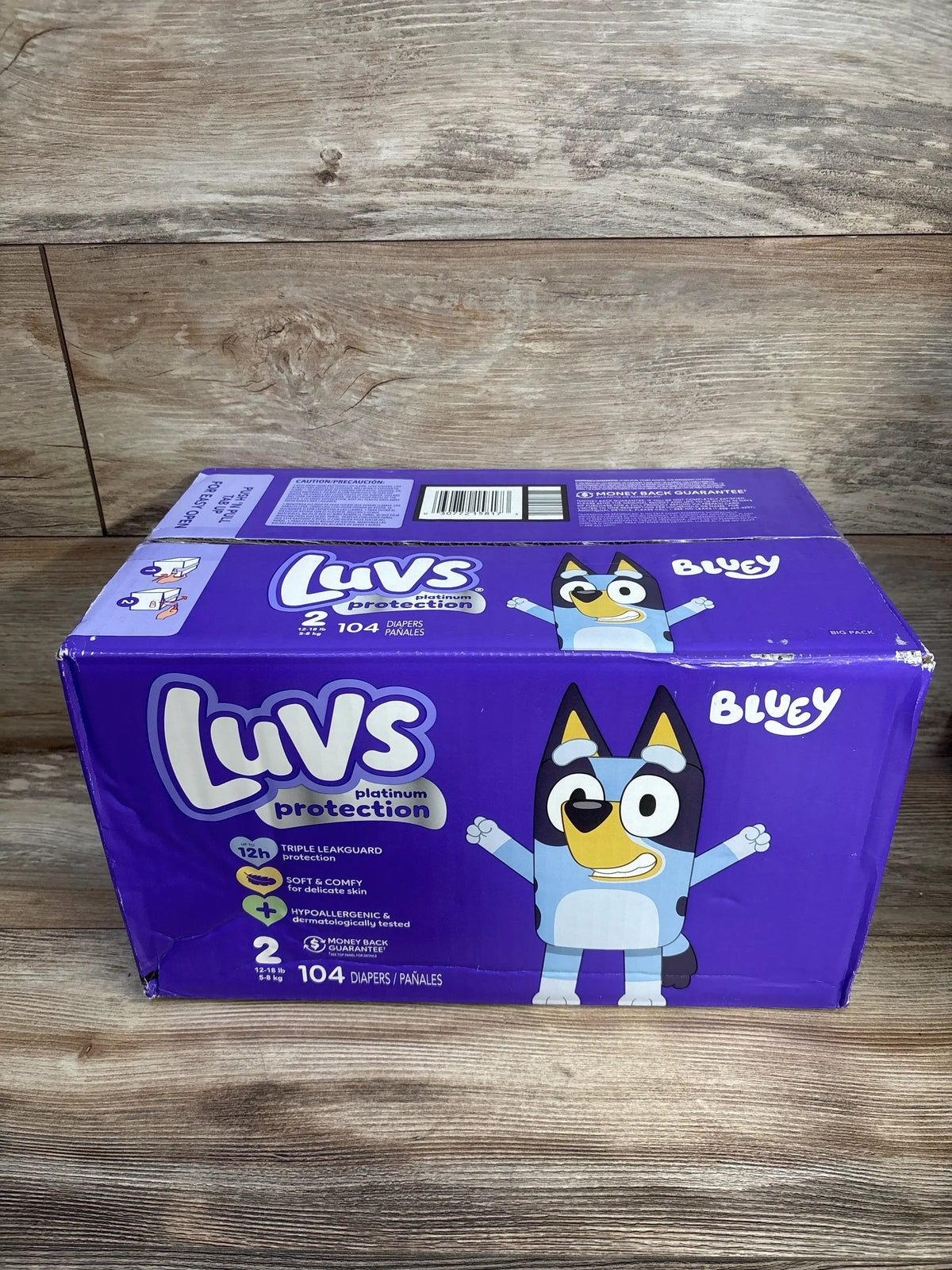 Front view of Luvs Platinum Protection Size 2 diaper box (104 count) showing Bluey character and branding on wooden tabletop