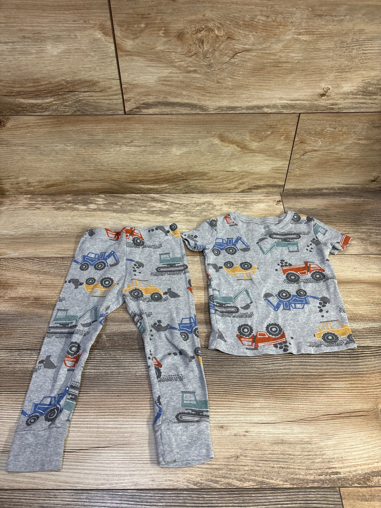 Front view of gray 2-piece construction vehicle pajama set with short-sleeve top and cuffed pants on wood background