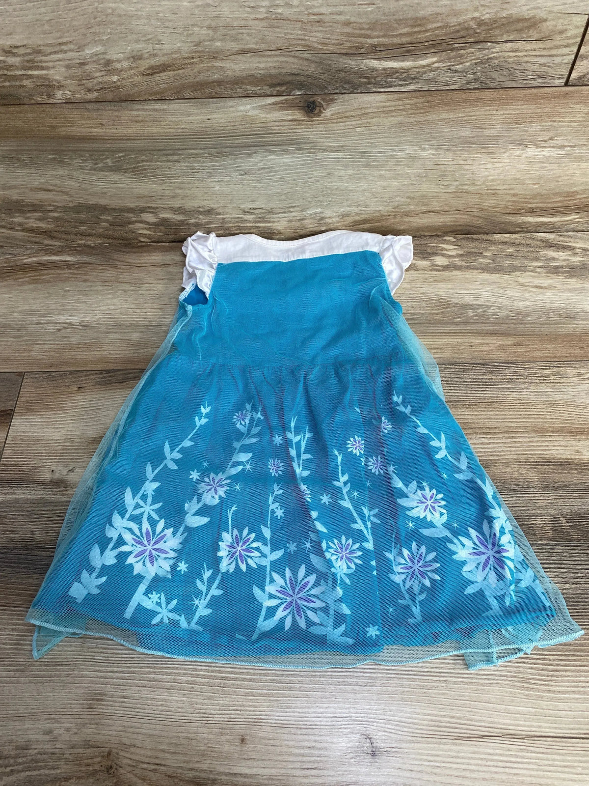 Front view of Floral Dress White/Blue sz 2T showcasing white sleeves and a blue floral skirt on a wood-grain background