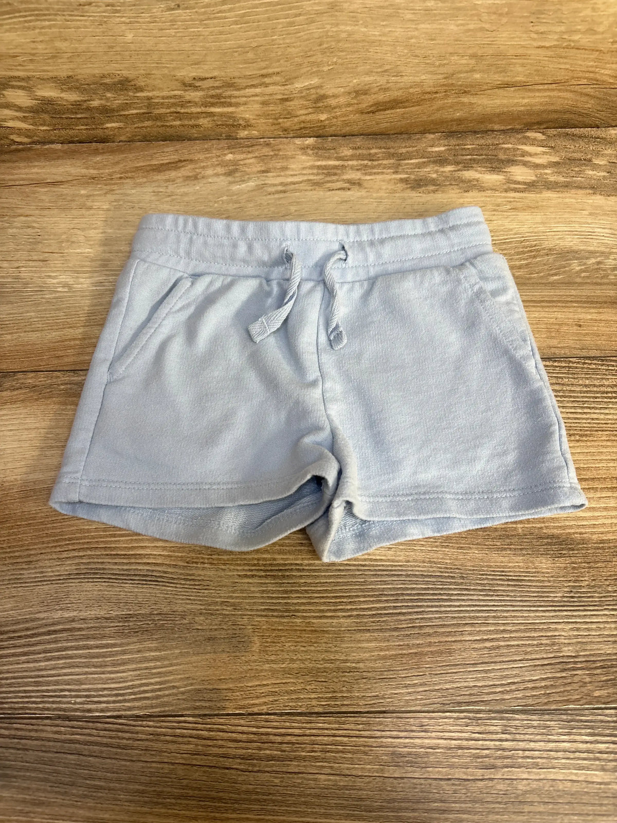 Flat lay of Cat & Jack blue cotton drawstring shorts showing elastic waistband, drawstring, and front pockets on wood