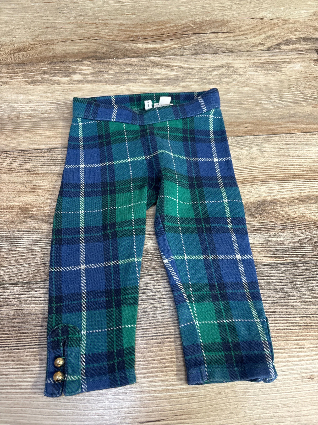 Green and blue plaid toddler pants with gold buttons on wood background