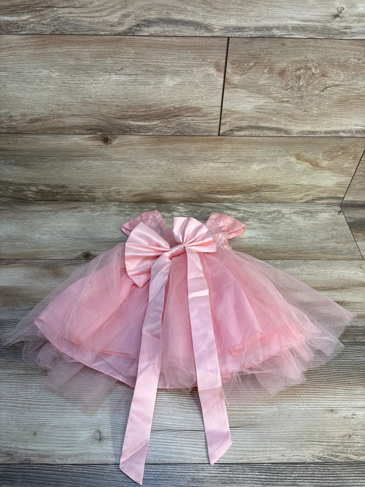 Pink tulle baby dress with short sleeves and large satin bow, displayed on wooden background