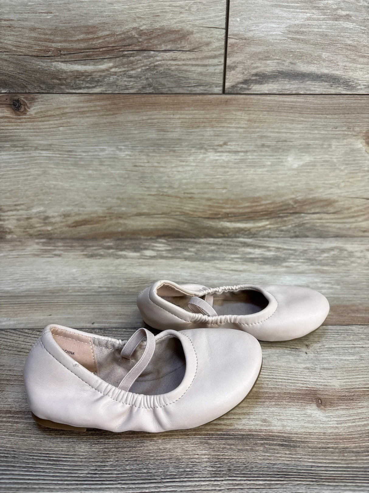 Light pink toddler ballet flats with elastic straps on wood floor
