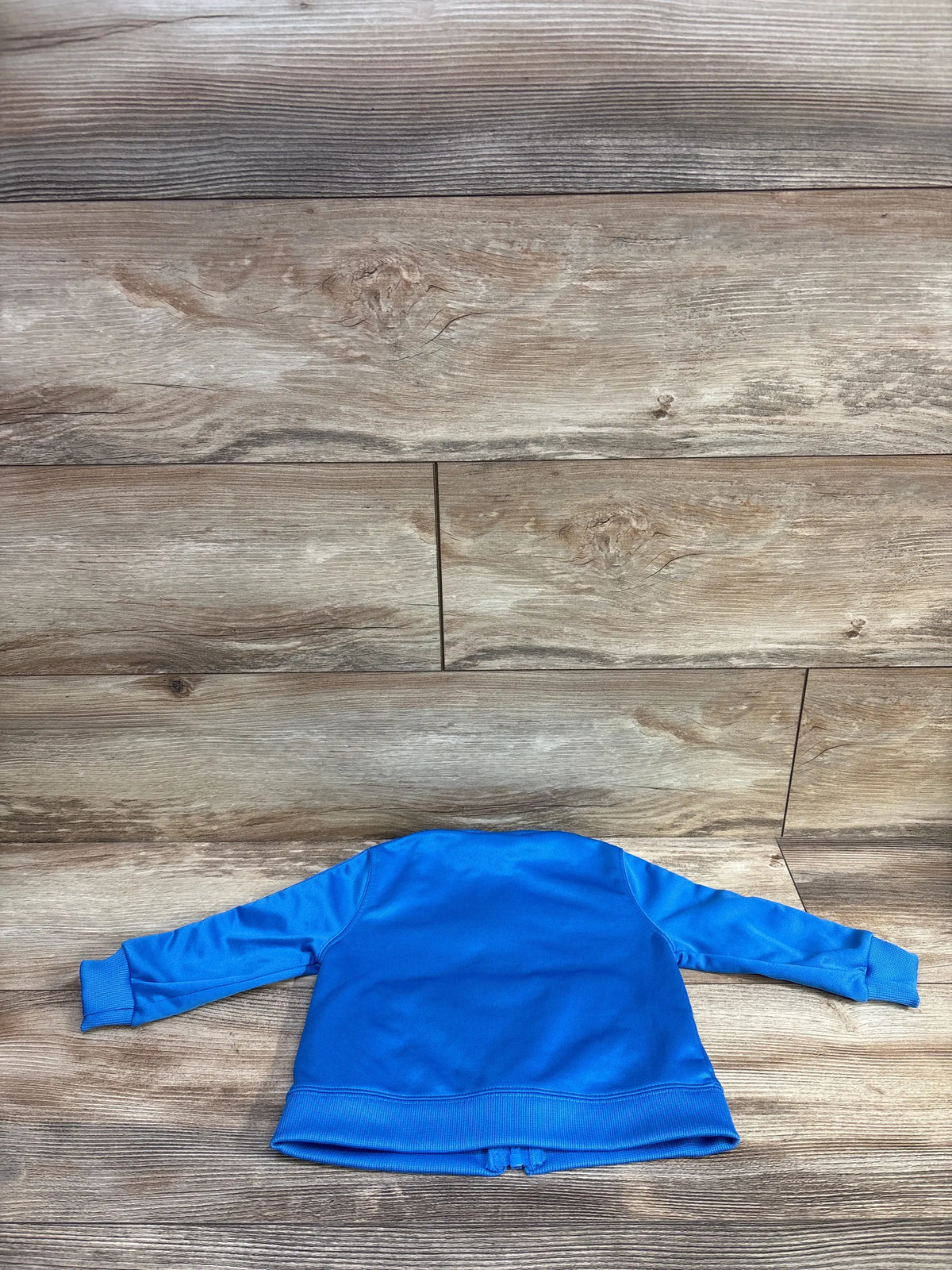 Back view of Nike full zip taped track jacket in blue showcasing ribbed hem on a wood-look floor