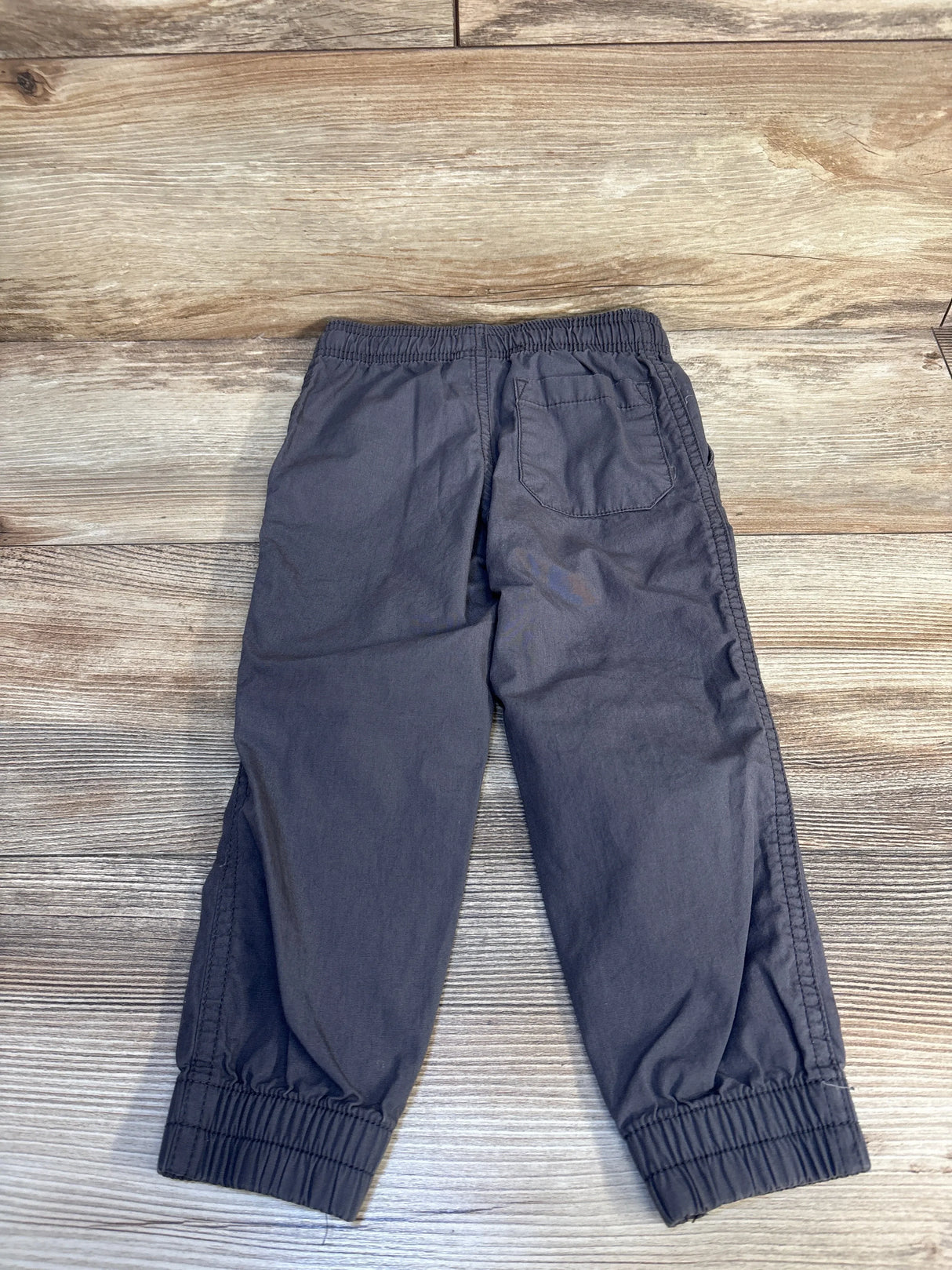 Gray toddler jogger pants with elastic waist and cuffs, back pocket, on wood floor