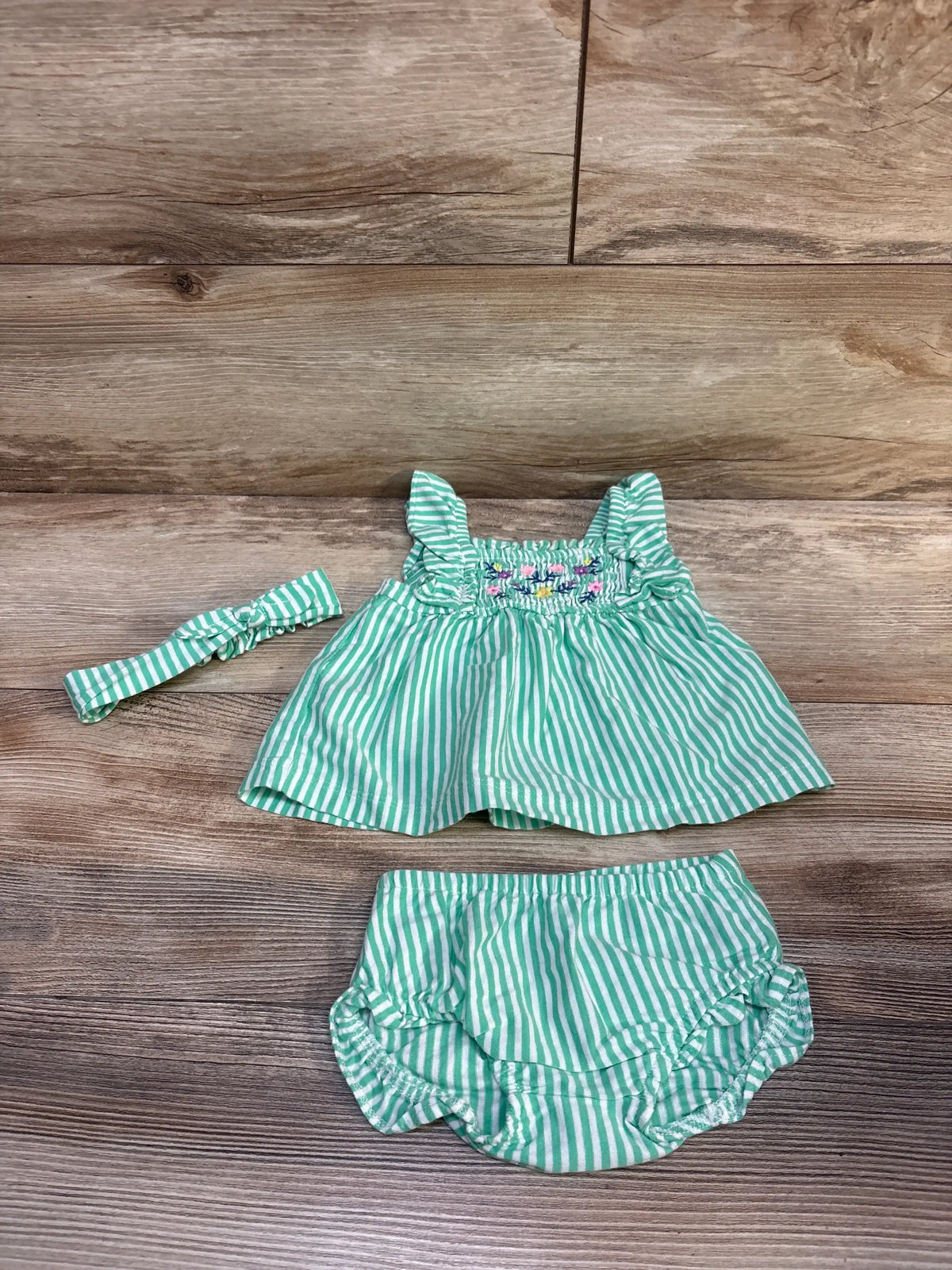 Front view of Carter’s 3pc striped set showcasing a smocked peplum top, matching bloomers, and head bow on a wood background