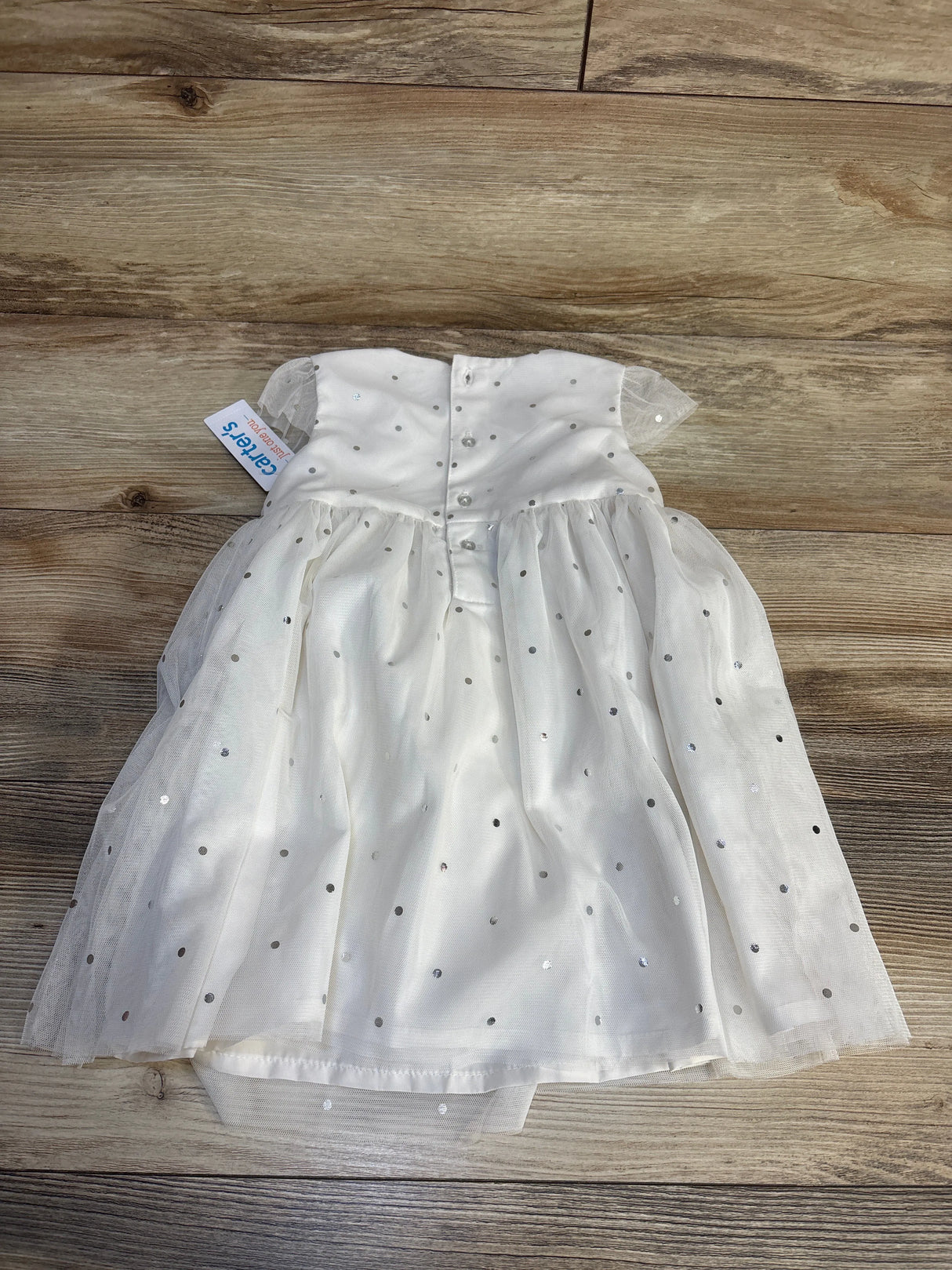 White baby dress with silver polka dots and buttons, laid on wooden floor