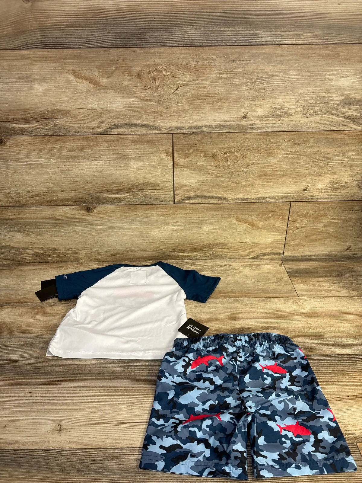 Flat lay of Hurley rashguard set 24m showing white shirt with navy sleeves and blue camo shorts with red shark print