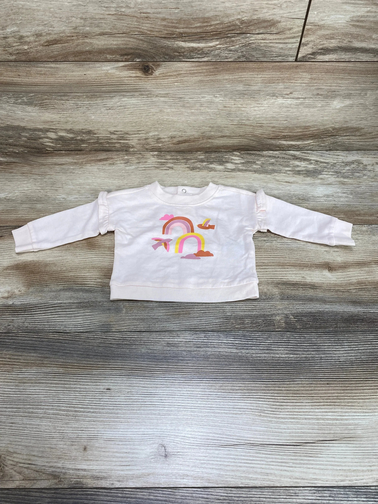 Front view of newborn pink Cat and Jack sweatshirt showcasing rainbow graphic and ruffle shoulder detail on wood background