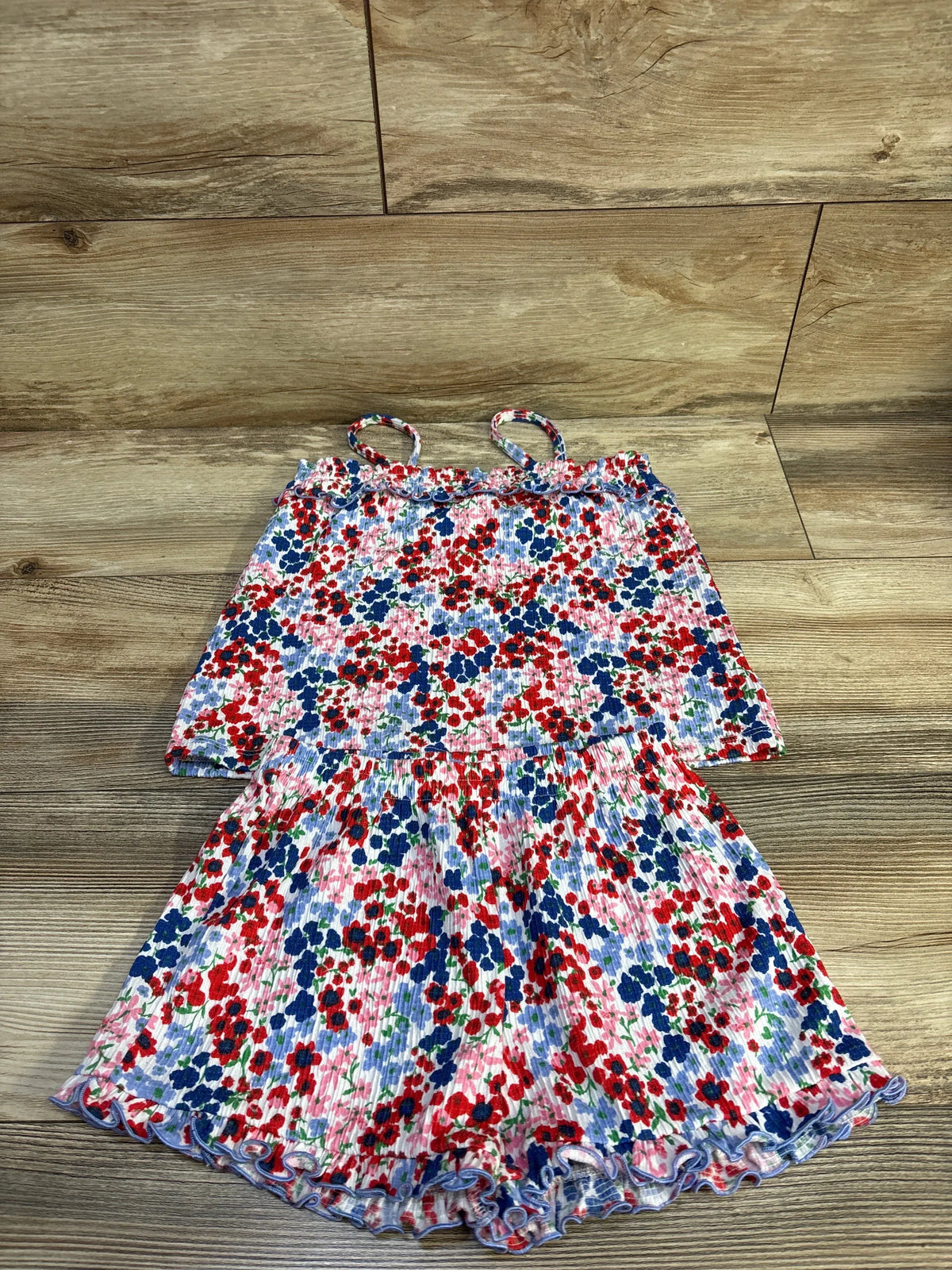 Flat lay of 2-piece toddler sleeveless ruffle top and shorts showing red and navy ditsy floral print on wood background, size 4T