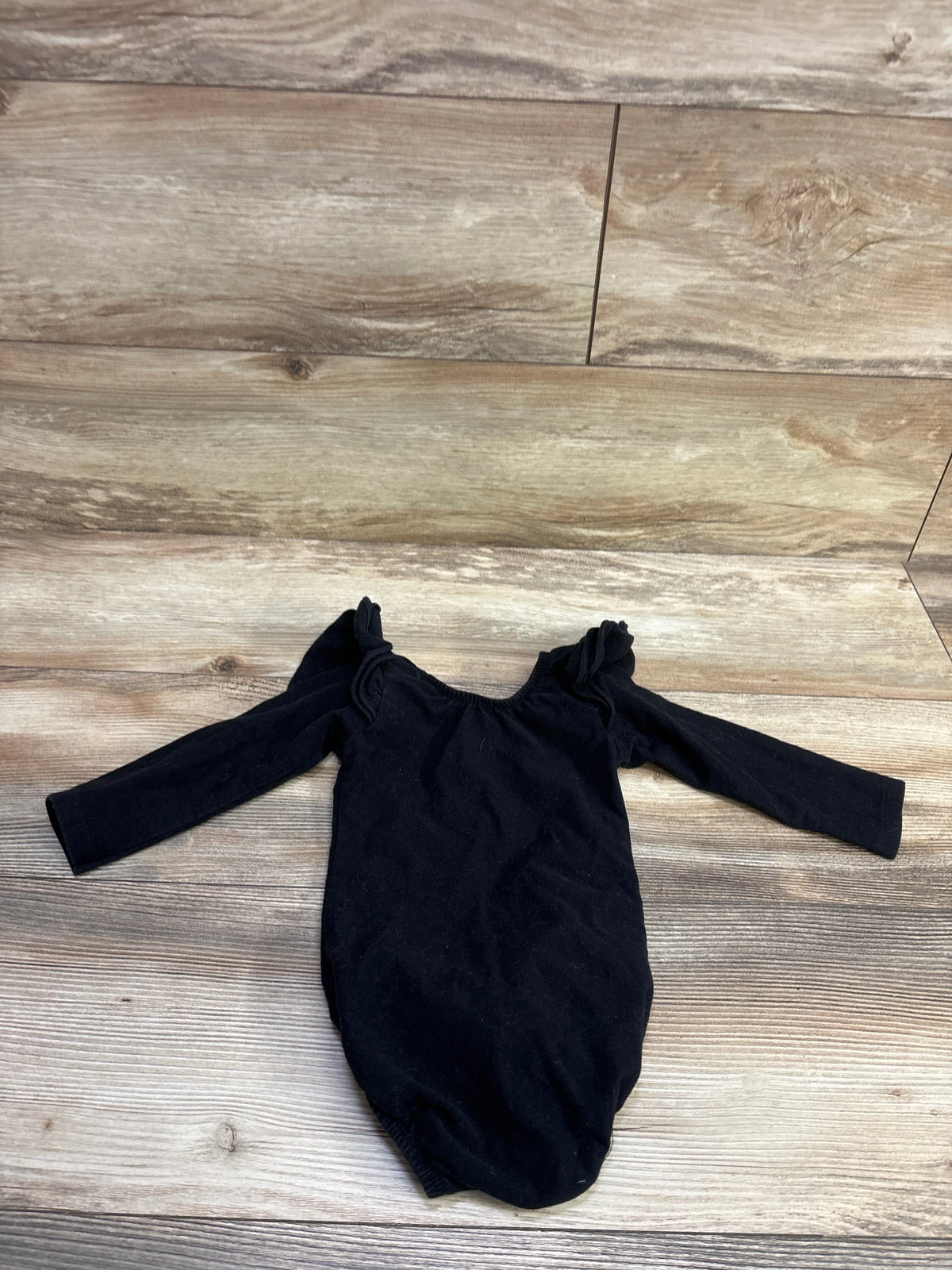 Front view of black long sleeve bubble romper showcasing flutter shoulder details with a wood-look floor background
