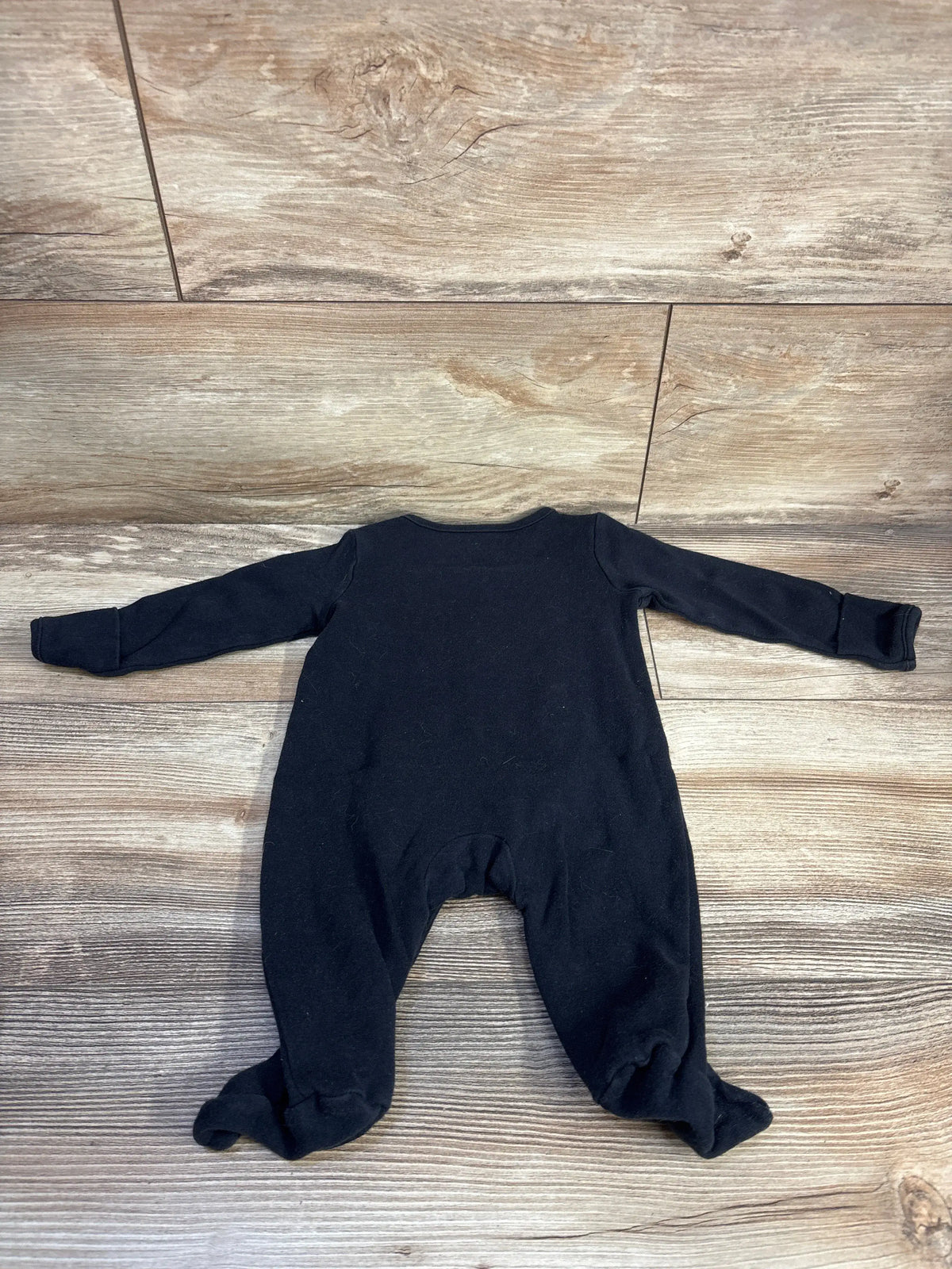 Flat lay of Just One You skeleton footed coverall in black with long sleeves on a wood-look floor