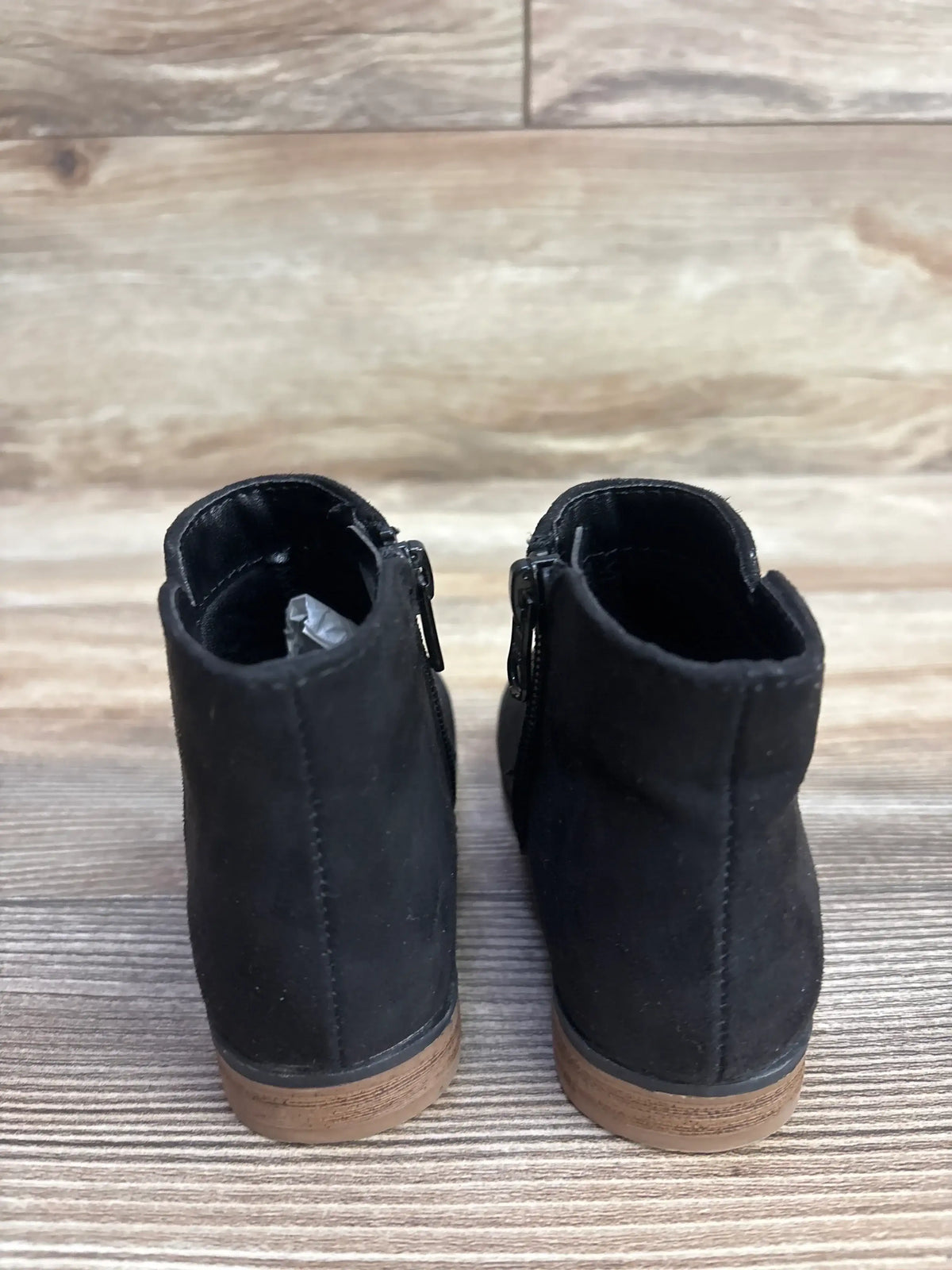 Pair of black toddler ankle boots with side zippers and brown soles on wooden floor