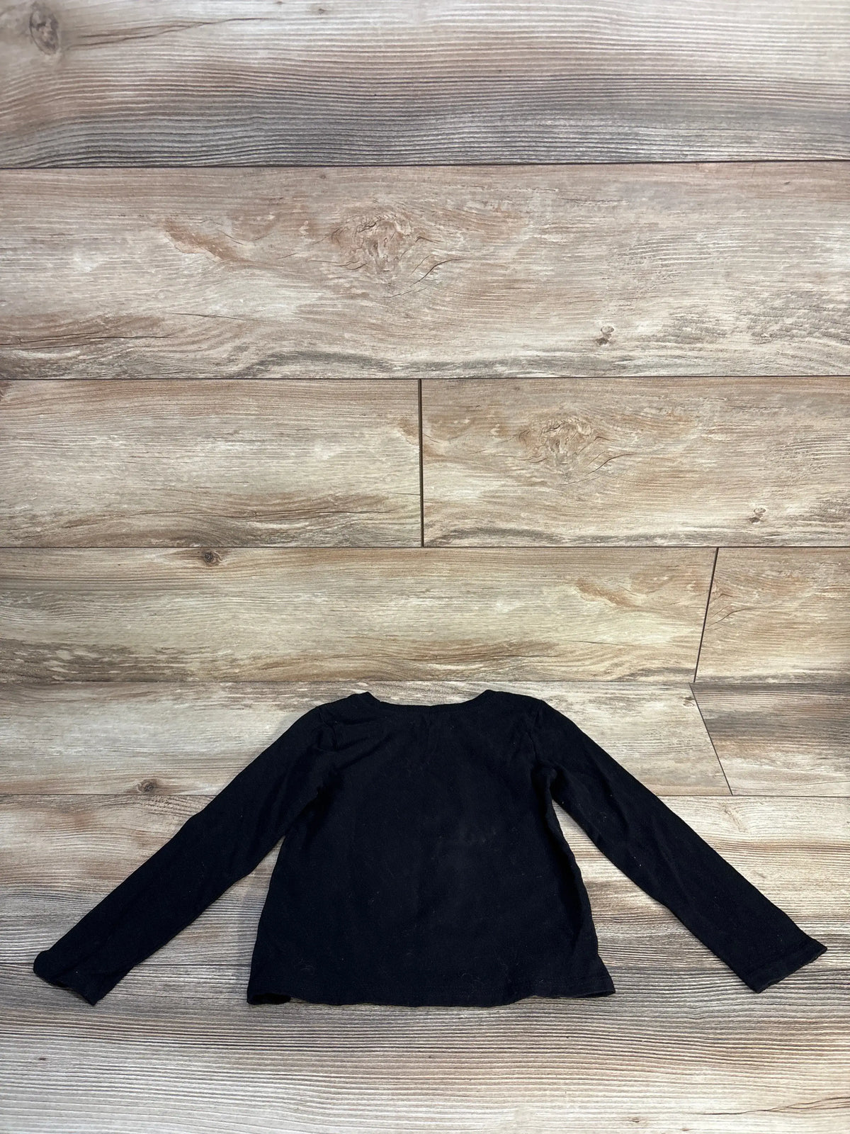 Back view of Children’s Place fall cat shirt showcasing black long sleeves with a wood floor background