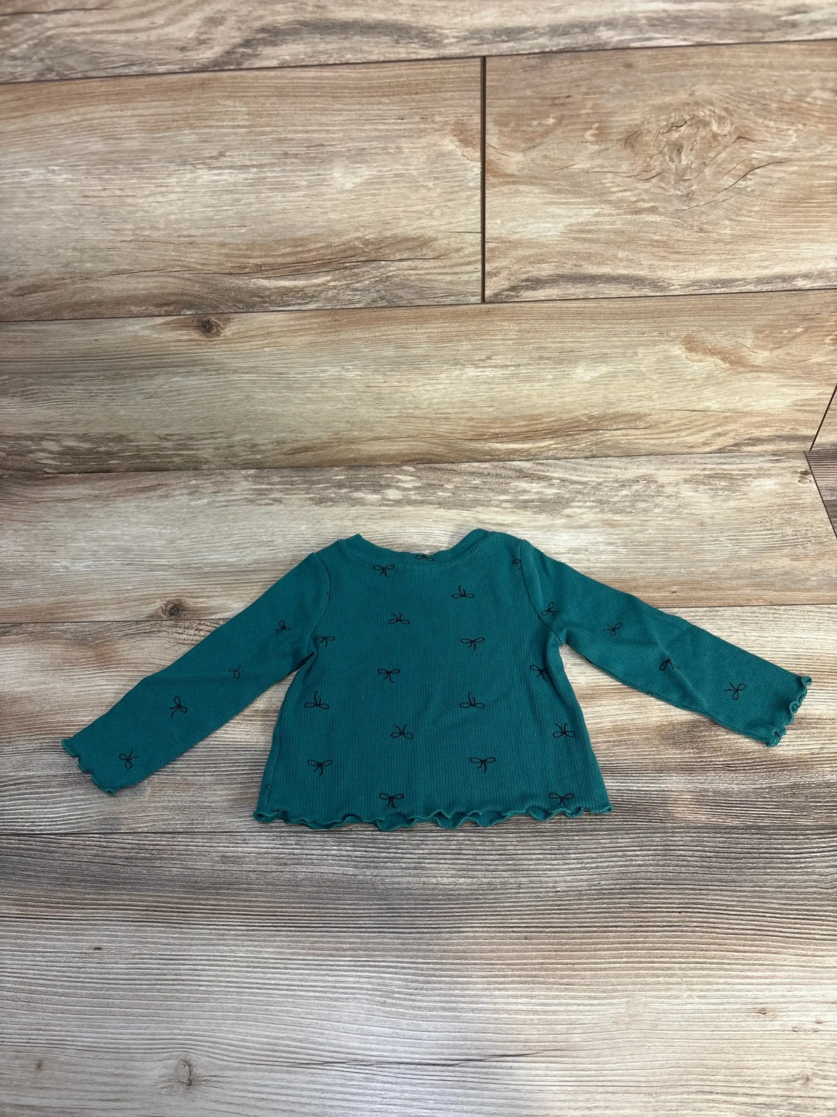 Teal long sleeve toddler shirt with black bow pattern on wood floor