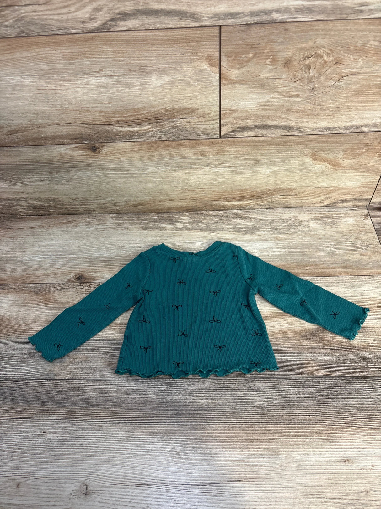 Teal long sleeve toddler shirt with black bow pattern on wood floor
