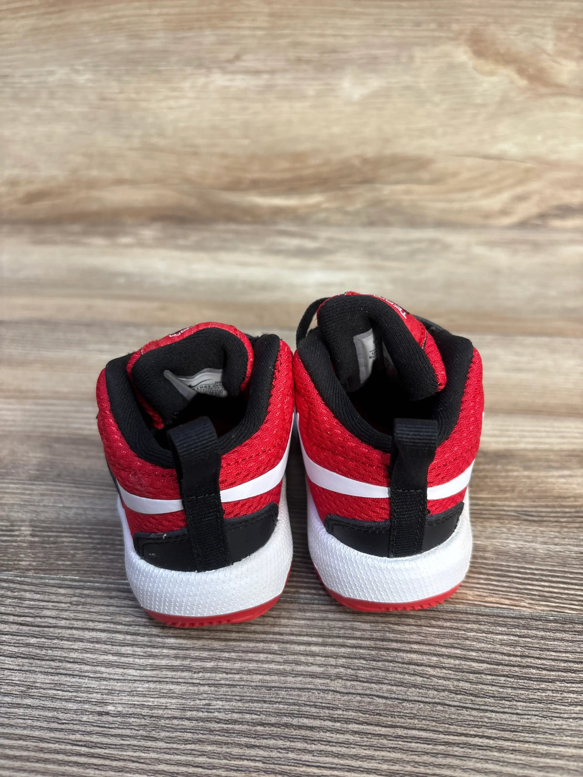 Rear view of Nike Team Hustle D8 Black University Red sneakers, size 5C, with white midsoles on wood grain