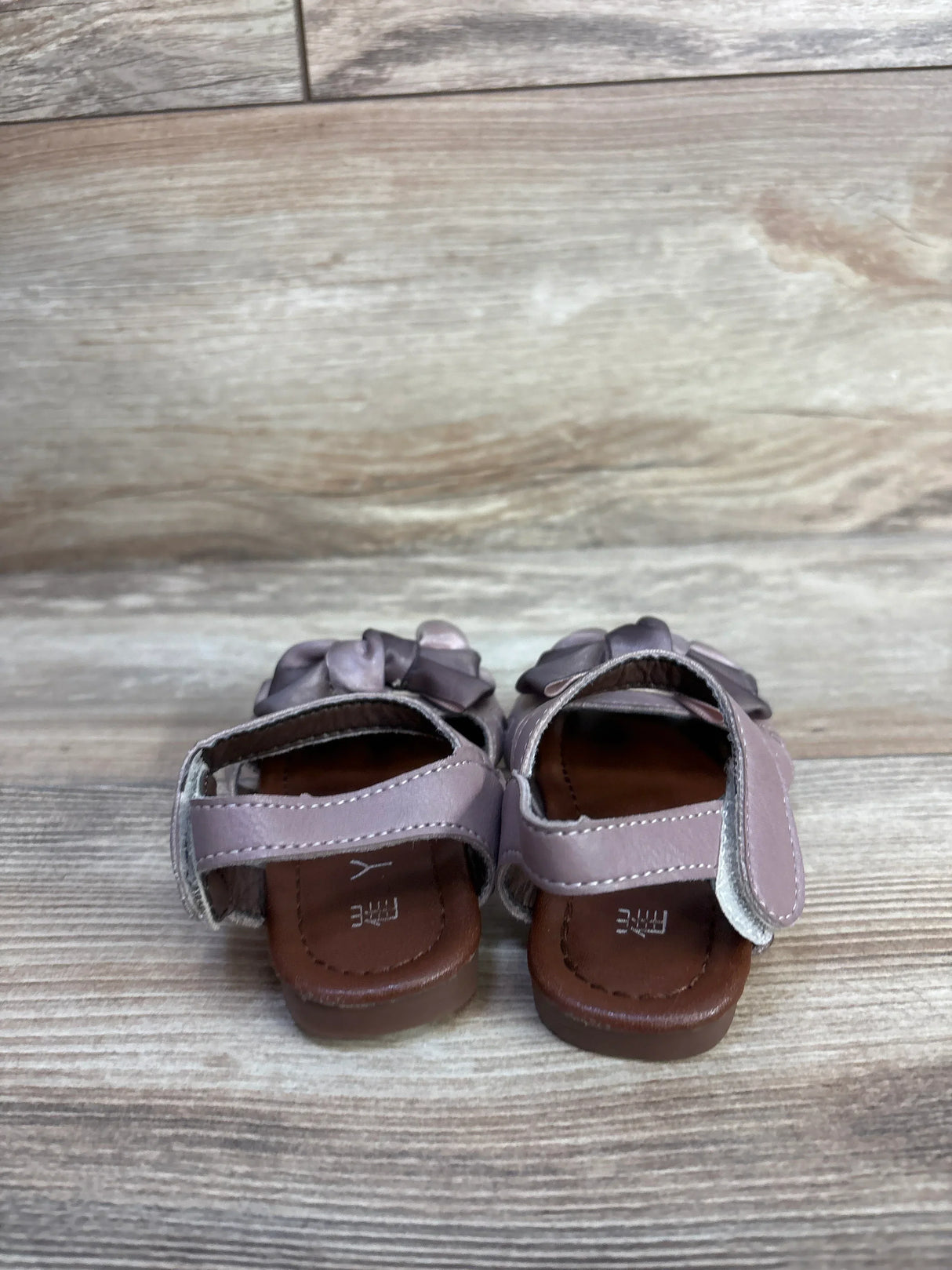 Rear view of EYY sandals in mauve showcasing velcro ankle straps and decorative bows on a light wood floor