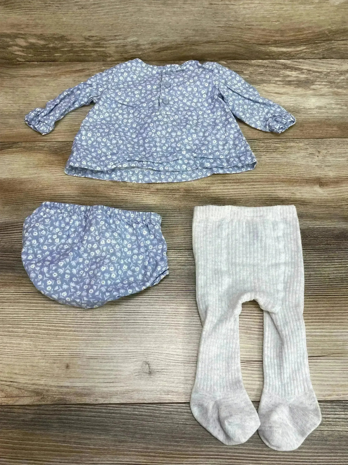 Flat lay of baby 3-piece outfit showcasing blue floral long-sleeve top with matching bloomer and ribbed light gray tights on wood floor
