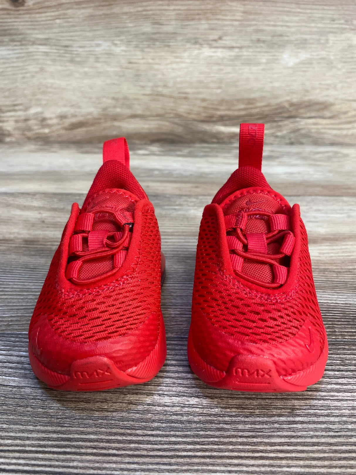 Red toddler Nike Air Max sneakers with mesh uppers on wood background