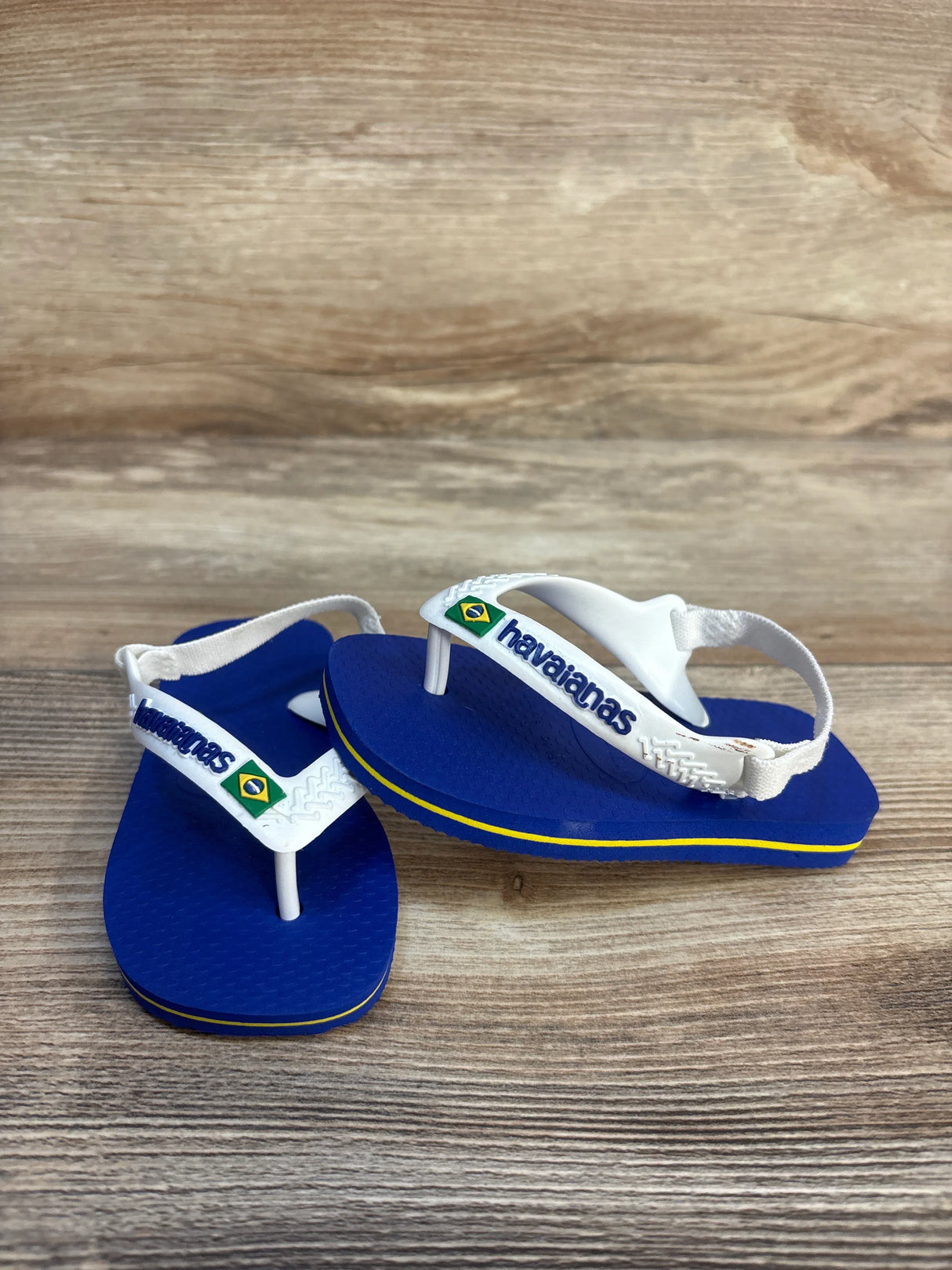 Blue toddler Havaianas sandals with white straps and Brazil flag, on wooden surface
