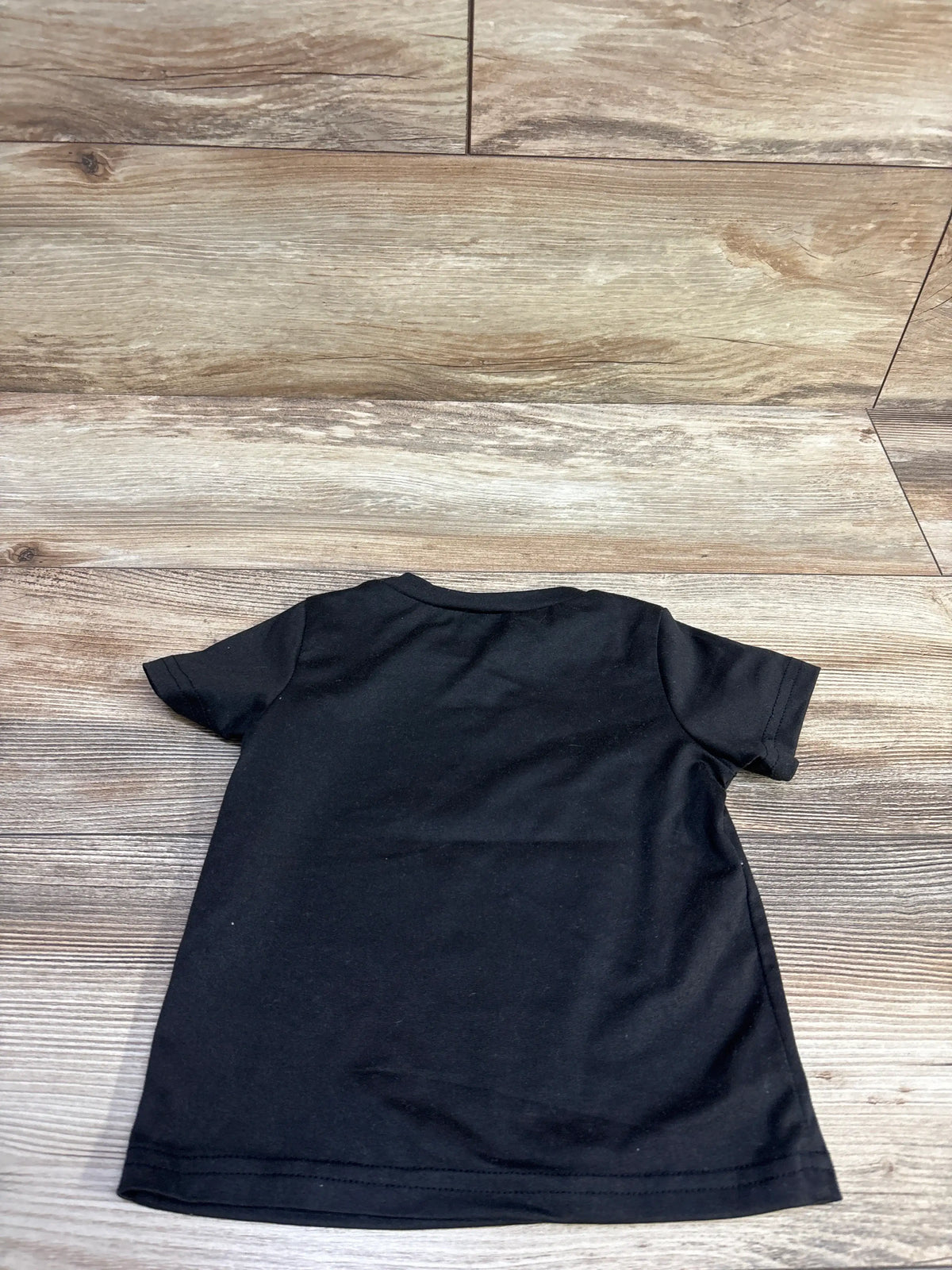 Back view of black Shein California shirt in size 12 to 18 months showcasing short sleeves on a wood floor
