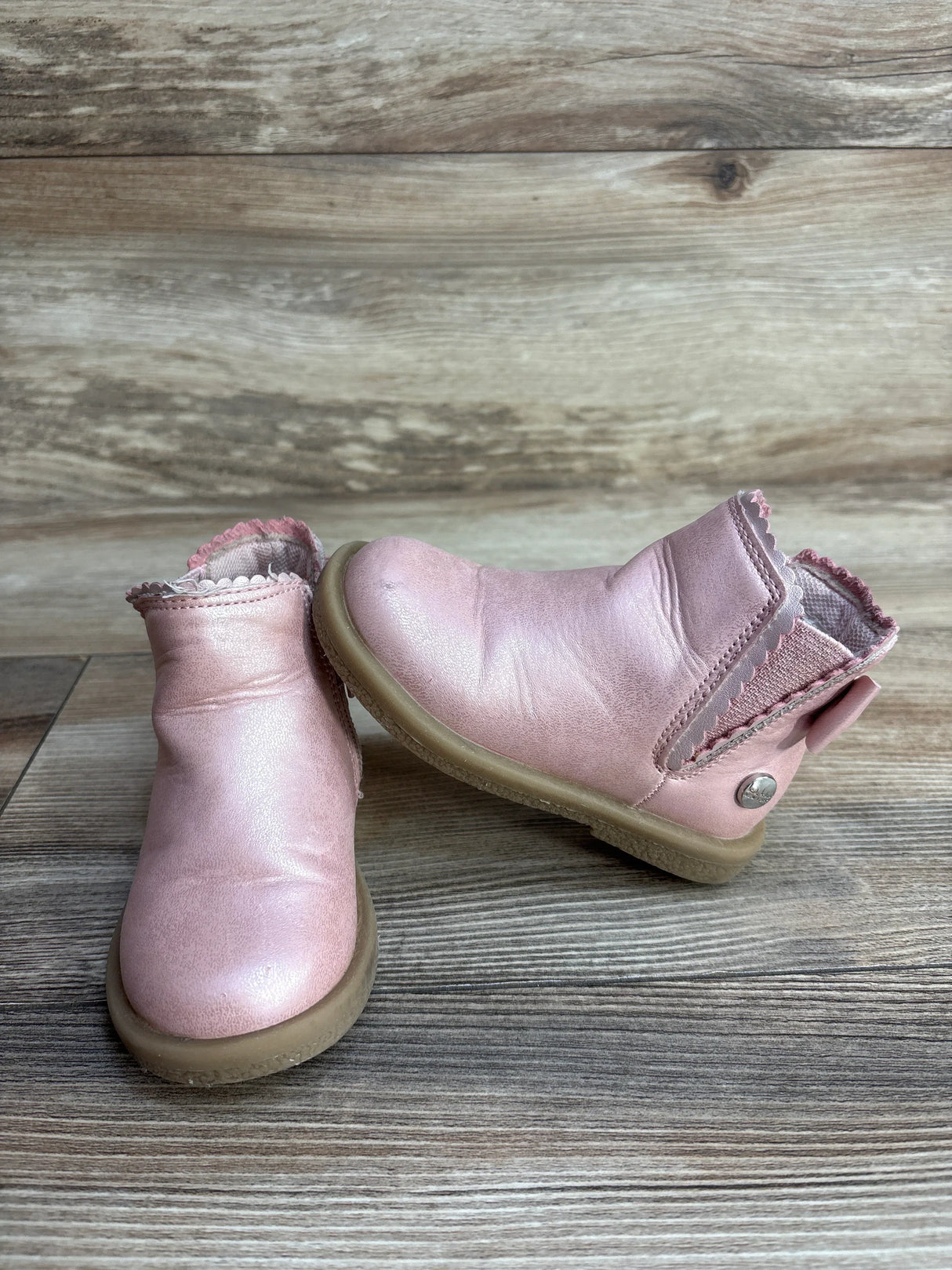 Pair of pink toddler leather boots with scalloped edges on a wooden floor