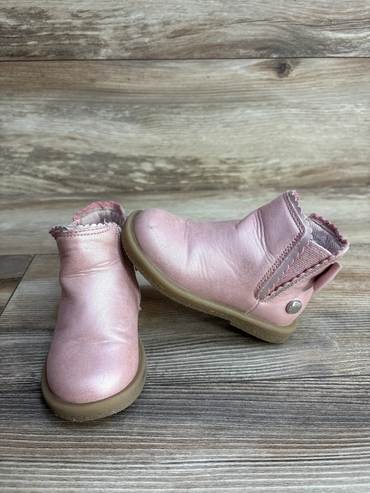 Pair of pink toddler leather boots with scalloped edges on a wooden floor