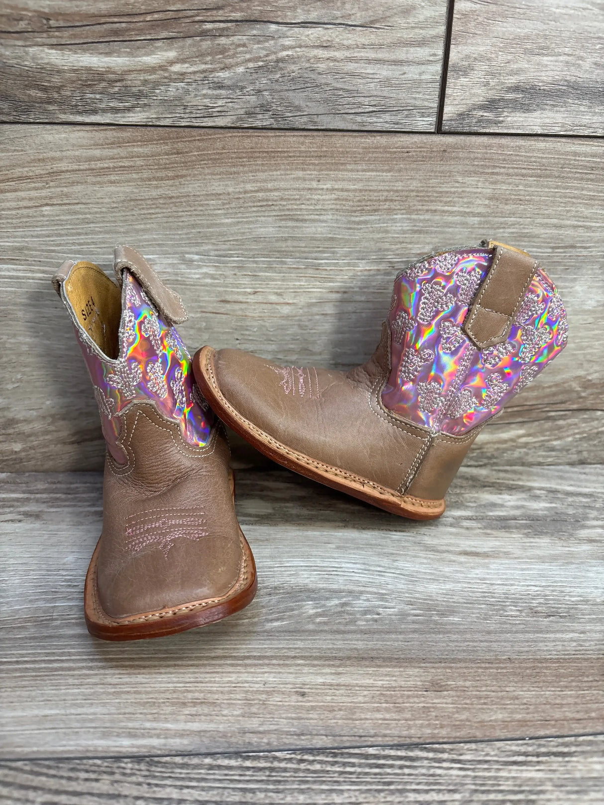 Front view of Roper Kids pink cowgirl boots, brown leather toe and holographic shaft with heart detail on wood background