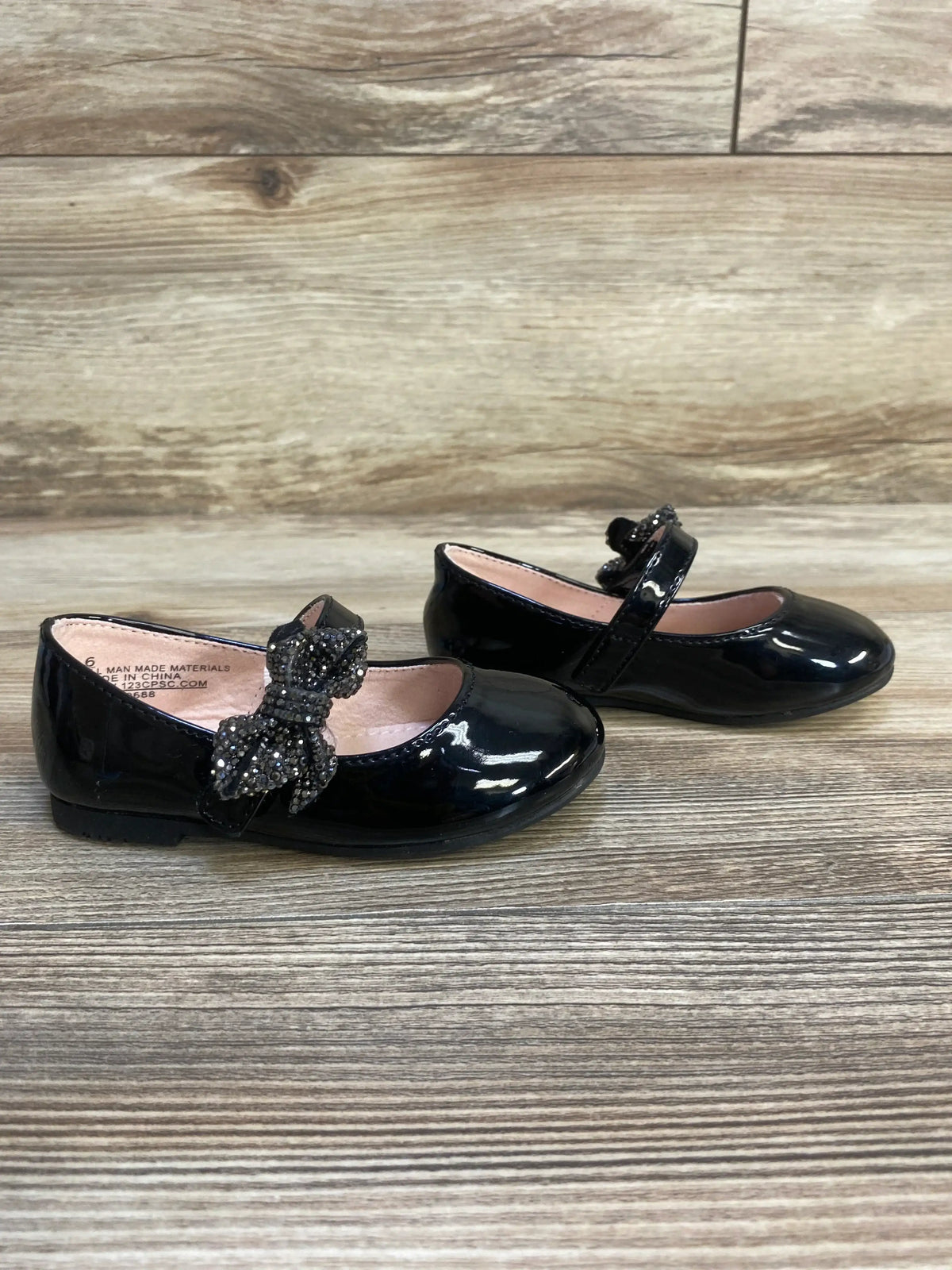 Black girls' patent dress shoes with sparkly bow strap detail on wood background