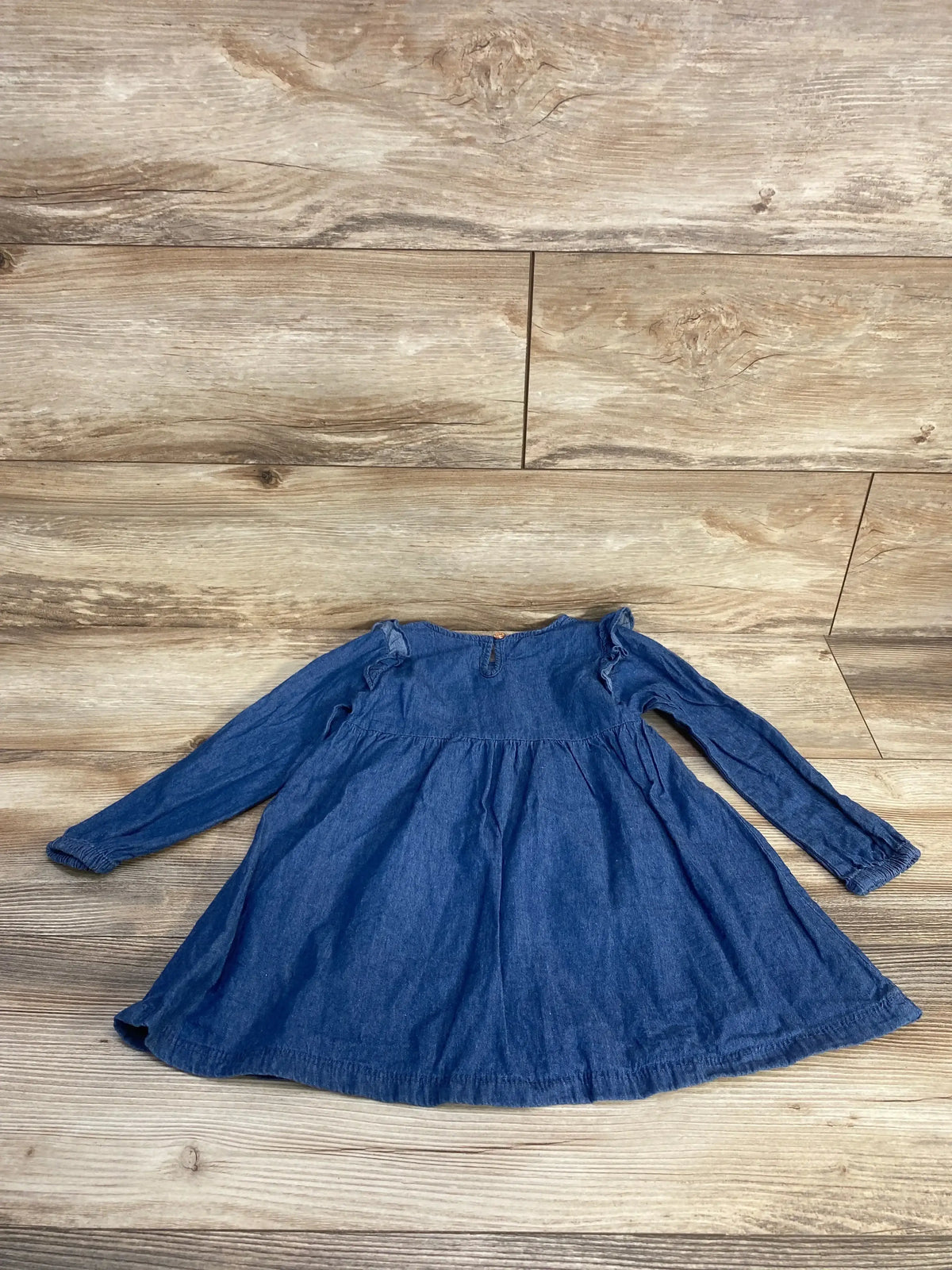 Flat lay of Vince Camuto chambray toddler dress showing long sleeves, gathered skirt and embroidered ruffled shoulders on wood