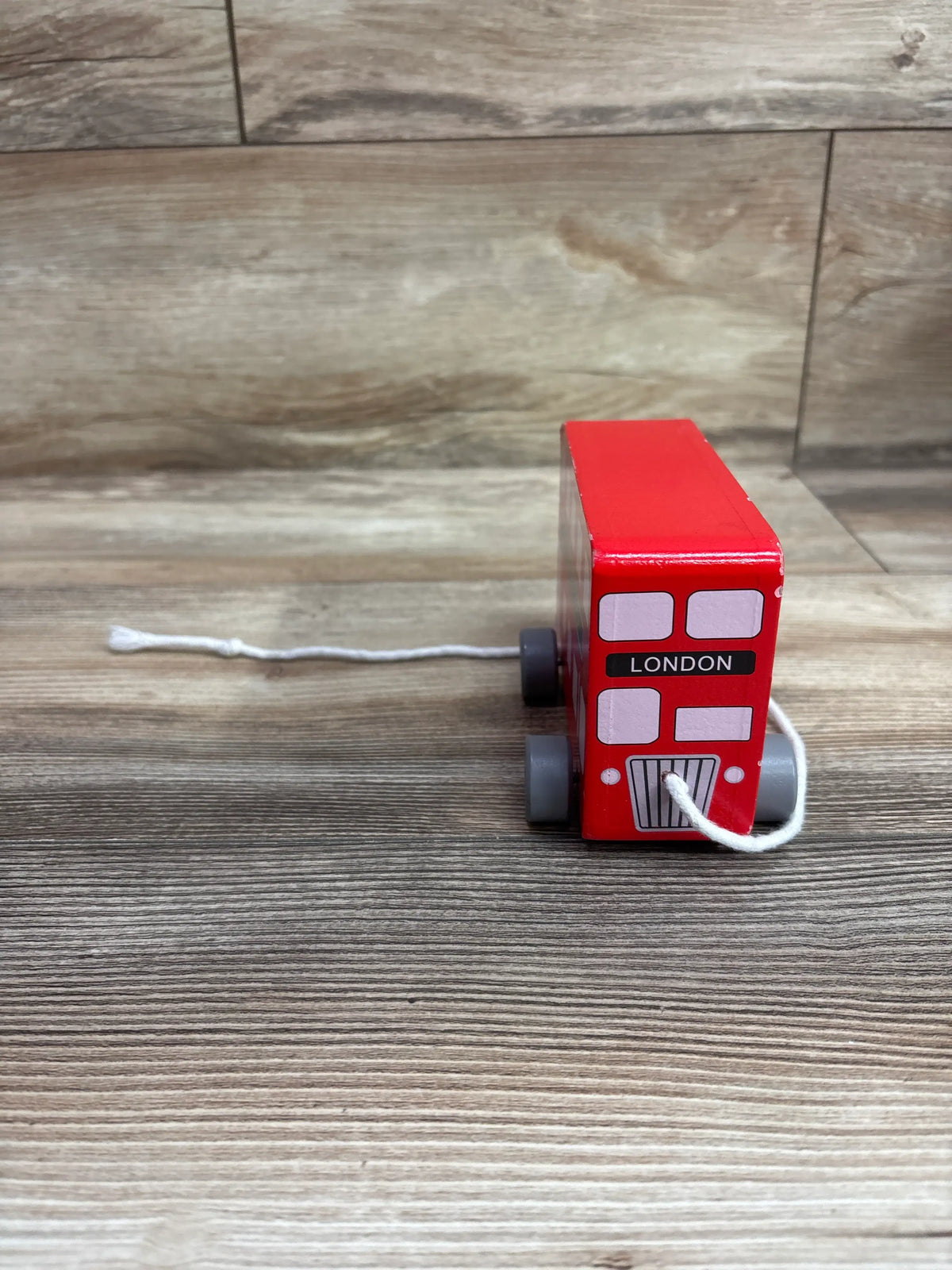 Front view of red London bus pull along toy showcasing its white pull string on a wood-look floor
