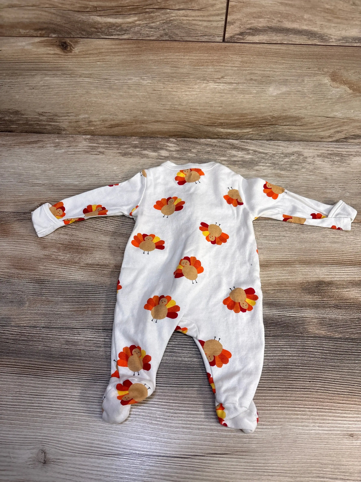 white baby onesie with colorful turkey print laid flat on wooden floor