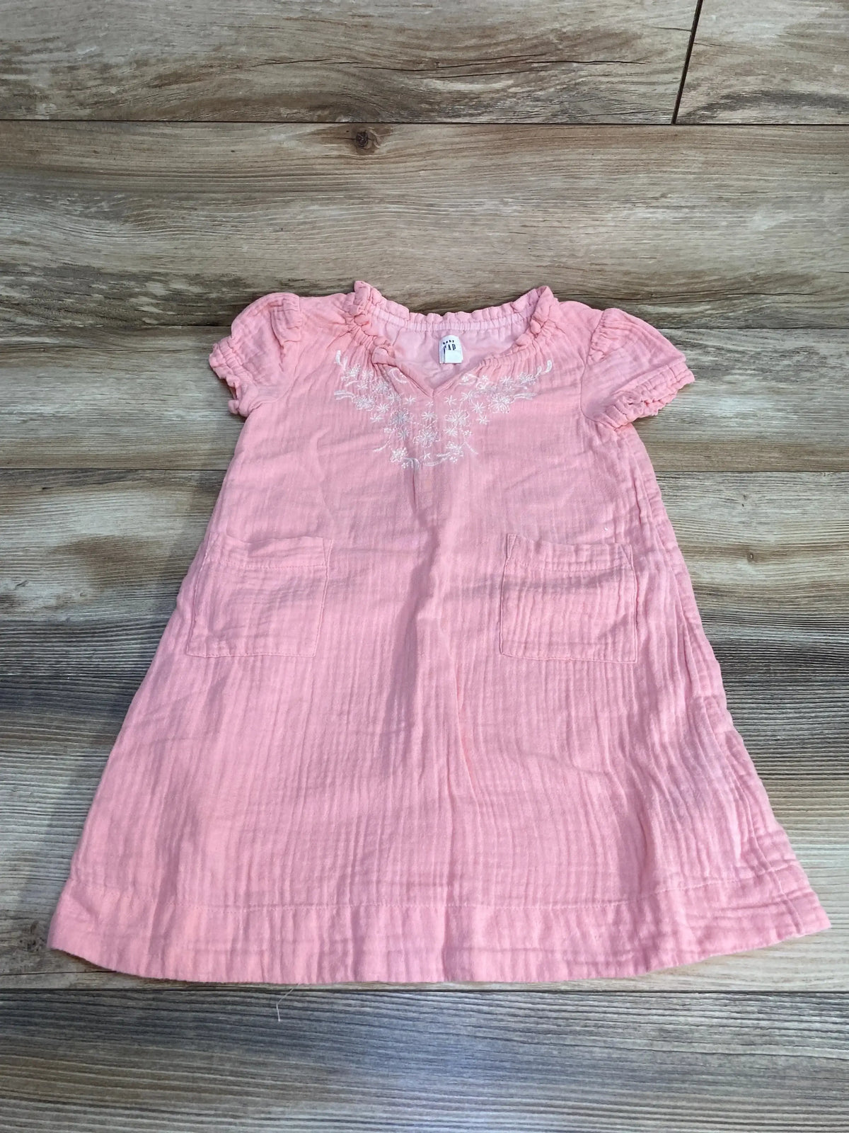 Top view of pink Baby Gap dress size 4T with embroidered neckline, puff sleeves and front pockets on wood background