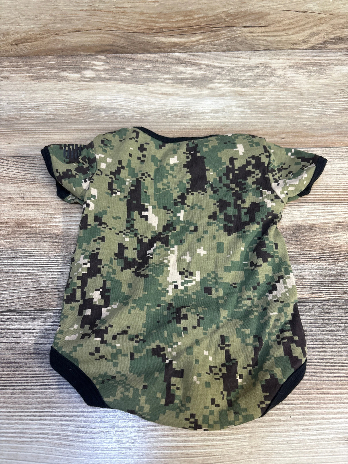 Green camouflage baby onesie with short sleeves on wood background