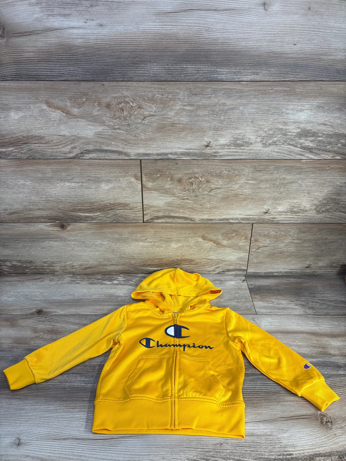 Front view of Champion full zip jacket in yellow, size 3T, showcasing hood, logo, and front pockets on wood grain