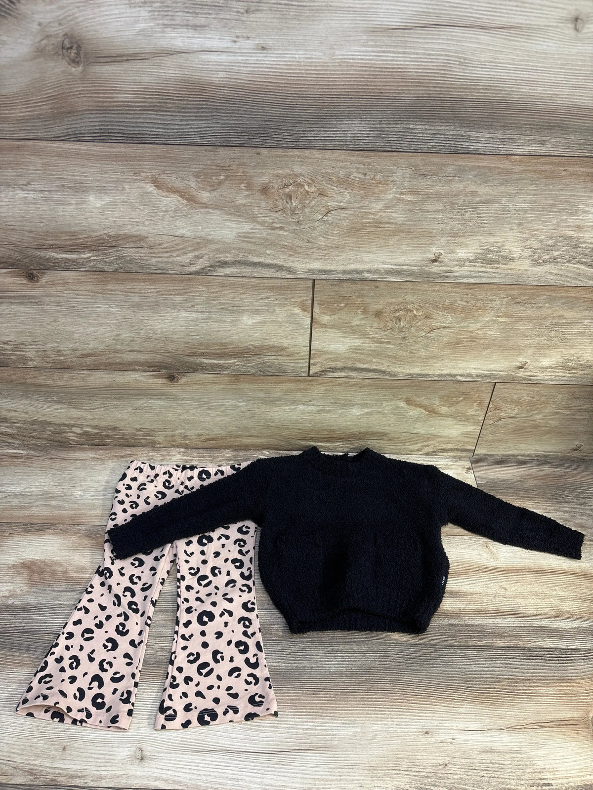 Top view of DKNY two-piece set showcasing black sweater and leopard-print flare pants on wood flooring