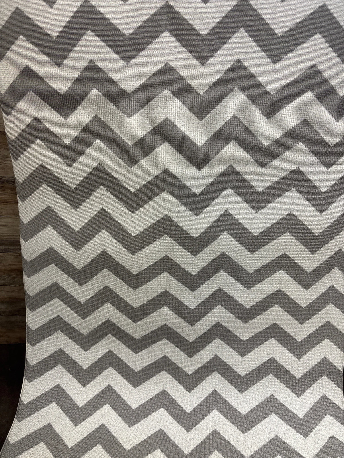 Close-up of Baby Care Play Mat Haute Collection showcasing a gray and white chevron pattern with wood floor background
