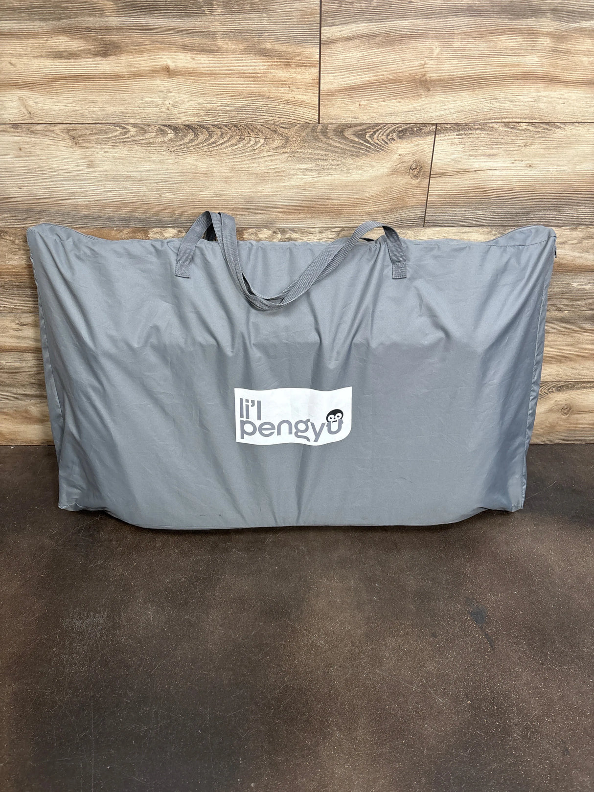 Gray Li'l Pengy portable baby gear storage bag with handles on wooden floor background