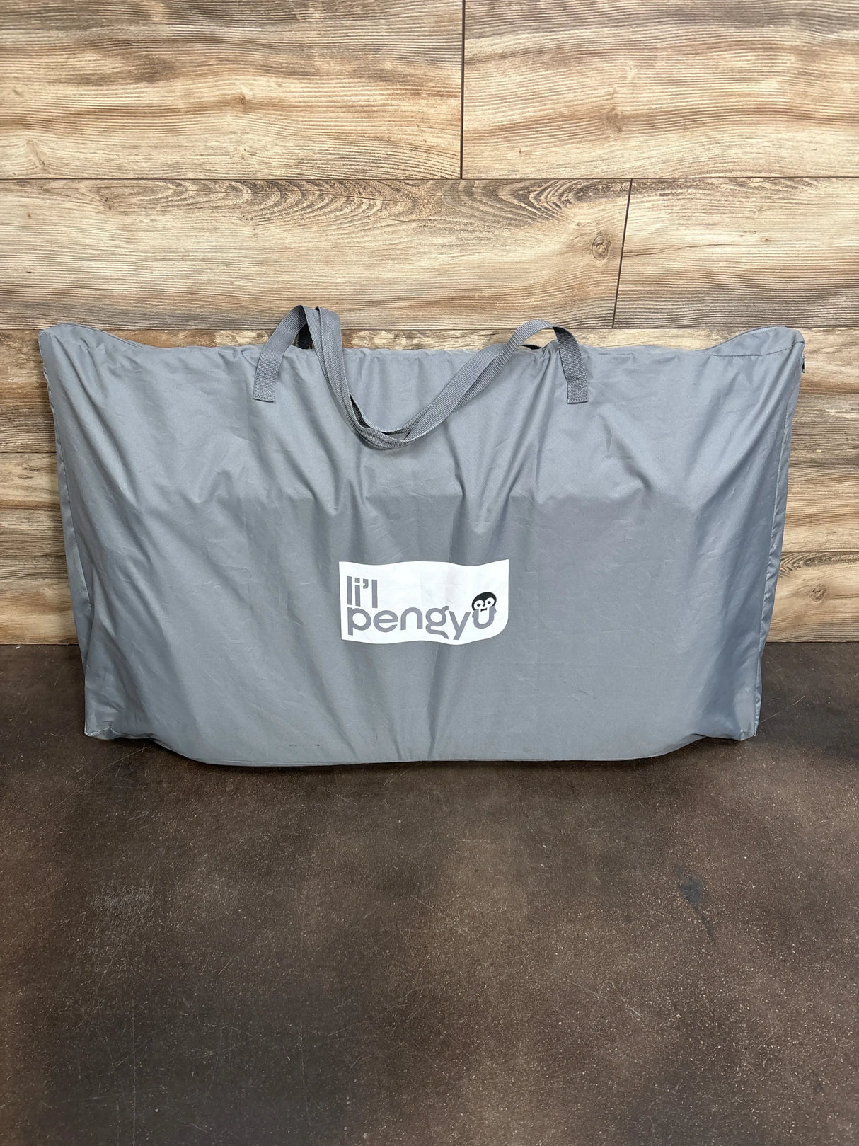 Front view of Lil Pengyu Bedtime Bliss bassinet storage bag showcasing grey carry tote with brand logo on wood plank floor