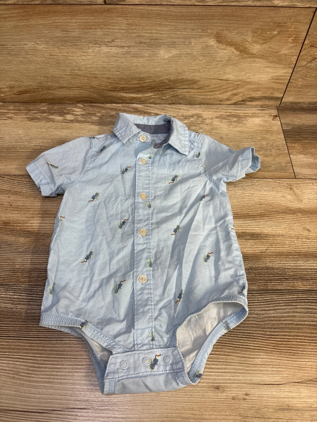 Front view of OshKosh blue bubble romper in size 12 months showcasing collared neckline, button front, and snap closure on wood