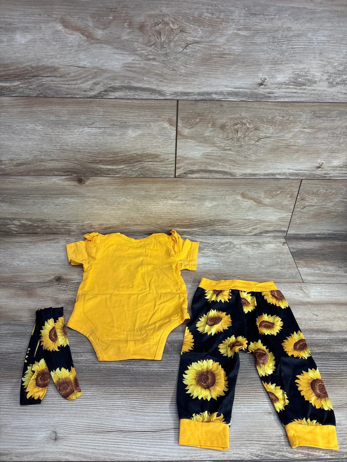 Yellow baby bodysuit with sunflower print pants and matching headband on wood floor