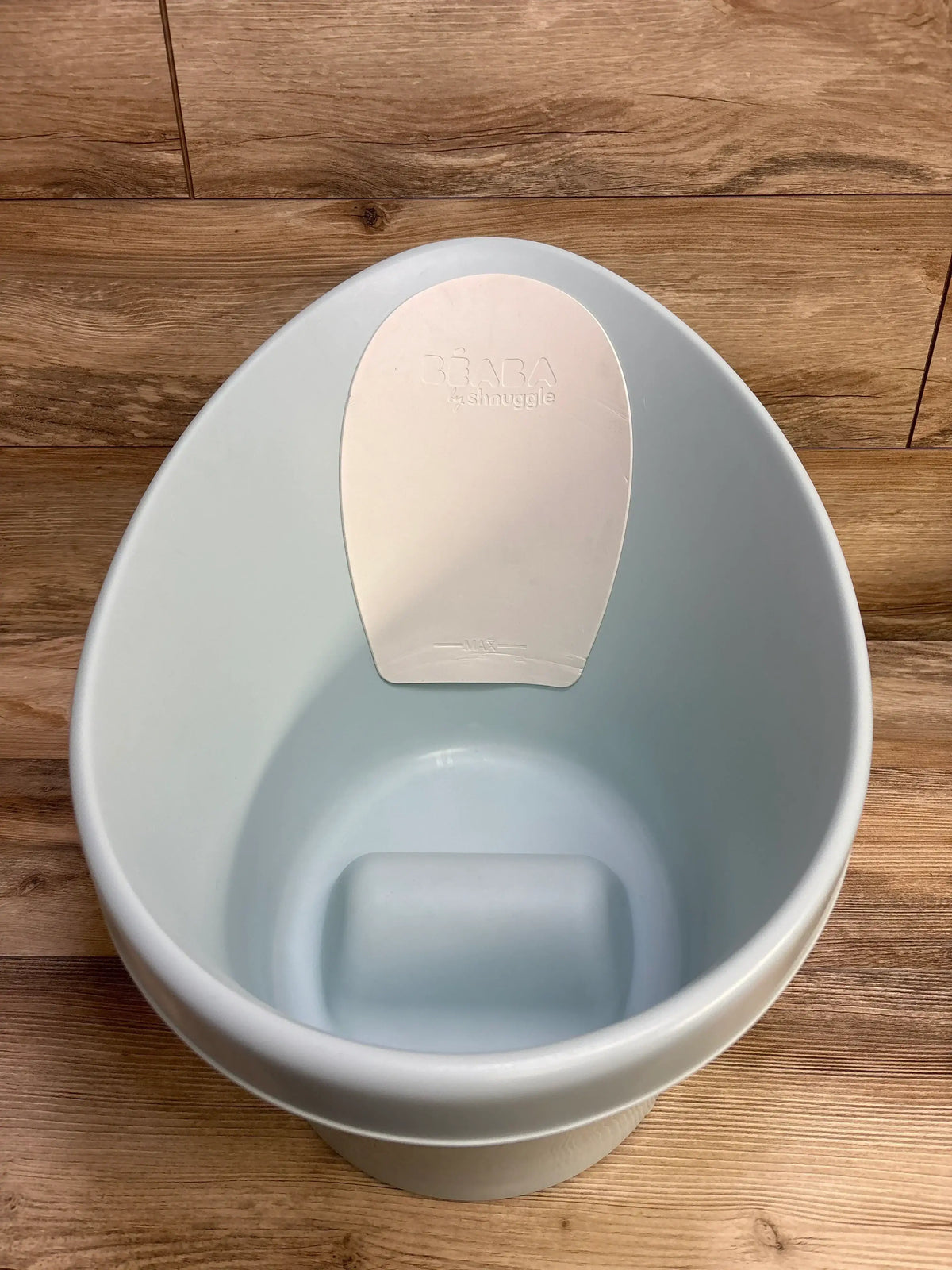 Top-down view of BEABA by Shnuggle baby bathtub, pale blue, showing ergonomic backrest and built-in seat on wood floor