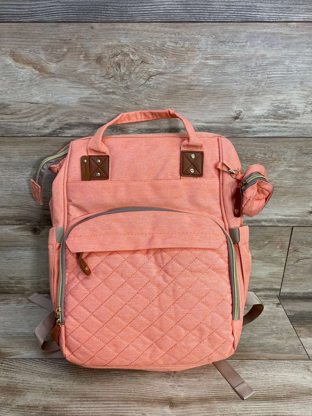 Coral pink quilted backpack with front pocket and leather accents on wooden floor